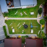 Widok z lotu ptaka na domki letniskowe Żeglarska Przystań w Chłapowie. Drewniane domki otaczają ogród z hamakami, stołami, trampoliną i placem zabaw.