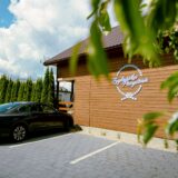 Samochód stoi na parkingu przy drewnianym budynku, którego ścianę oznacza duże logo Żeglarska Przystań.