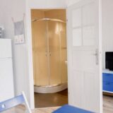Widok z salonu na otwartą łazienkę z kabiną prysznicową – układ wnętrza domku letniskowego w Chłapowie.