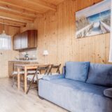 Drewniany salon domku z niebieską sofą, stołem i krzesłami oraz obrazem przedstawiającym zejście na plażę.