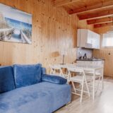 Drewniany salon w domku letniskowym z niebieską sofą, stołem i krzesłami oraz obrazem przedstawiającym zejście na plażę.